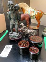 Wide view of lot showing large ceramic horse statue, smaller metallic horses, smiling man statue with child, and three decorative trinket boxes on a table.