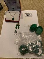 Overview of all items laid out, showing necklace, pendants, ring, cabochons, and sealed bag of jade rings