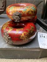 Two red lacquer donut-shaped jewelry boxes stacked, showing exterior motifs and hardware