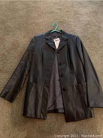 Front view of the dark brown leather coat laid flat on a beige carpet, showing four front buttons, two pockets, and smooth lambskin leather material.