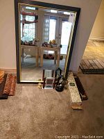 Framed mirror leaning on wall with items placed in front on the floor including clocks, shoe brush box, and tierack.
