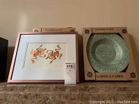 Framed signed Bill Reid print next to The Origin of Light decorative plate in original box.