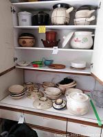 Full view of cabinet shelves stocked with various ceramic pots, bowls, and pottery items in mixed sizes and styles.
