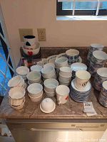 Collection of various ceramic ramkins and cups including poker-themed cups and floral bowls arranged on countertop.