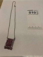 Full view of silver chain necklace with rectangular red stone pendant.