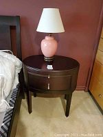 Oval dark wood table with drawer and sliding board, showing scratches and worn condition, placed near bed and dresser.