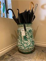 Full view of the white ceramic umbrella holder with green floral and bird decorations filled with umbrellas.