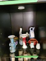 Shelf of various ceramic items including vases, bowls, and statues in a black display case.