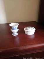 Miniature Wedgwood vase next to small lidded trinket dish on wood surface.