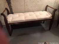 Wood-framed bench with upholstered beige seat and button tufting, shown from the front against a basement wall.
