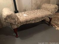 Side angle view showing floral patterned upholstered bench with two rolled ends and dark wood legs.
