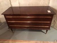 Front view of the cedar chest showing the smooth top surface, mid-century style legs, and front panel with horizontal handles.