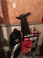 Toro Ultra electric blower vac with pipe attachments and original box next to Wilson Staff golf bag against basement wall.