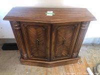 Wood cabinet front view showing carved decorative columns on the sides and double doors with brass handles.