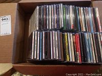 Overhead shot of cardboard box filled with cassette tapes and CDs, arranged vertically with spines visible.