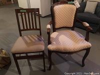 Front view of two chairs: one armchair with beige upholstery and wooden carved legs, one side chair with beige upholstered seat and wooden slatted back.