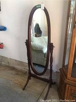 Front view of oval cheval mirror with wood frame showing full reflective surface and stand.