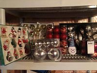 Various vintage Christmas ornaments in original packaging, displayed on shelving including birds, snowmen, and other characters as well as shiny balls in different sizes and colors