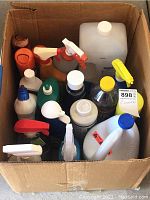 Top view of a cardboard box filled with various bottles of cleaning chemicals including a large white Clorox bleach bottle and multiple spray bottles.