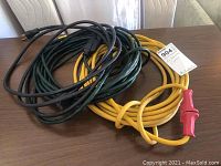 Three extension cords coiled on a table, colors black, green, and yellow with a red plug visible.