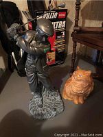 Full view of ceramic cat figurine and resin golfer figurine next to a box showing scale.