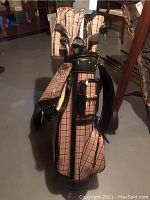 Photo showing beige and brown plaid Etto golf bag with black trim and attached cover in basement setting.