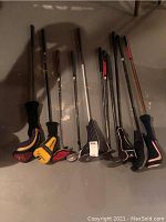 Full lineup of left-handed golf clubs with headcovers on concrete floor