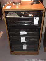 Front view of Technics wood media cabinet with glass door, containing audio equipment inside, showing logo and glass panel door.