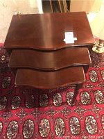 Three wooden nesting tables stacked together, showing dark finish and curved edges, on patterned rug.