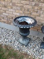 Outdoor resin planter with visible paint flaking on rim and interior, filled with soil, located beside a brick wall on gravel.