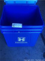 Photo of one blue plastic rectangular recycling bin with open top, featuring Hamilton logo in white on the front. Bin shows signs of weathering.