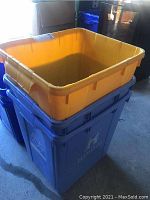 Three large blue plastic recycle bins, each with a removable yellow insert bin, stacked in garage.
