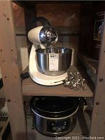 Sunbeam Mixmaster Heritage Series stand mixer with stainless steel mixing bowl and six metal beaters/hook attachments alongside an oval Hamilton Beach stainless steel slow cooker with digital display.