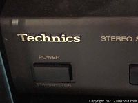 Close-up photo of Technics logo and stereo synthesizer tuner power button in black unit.