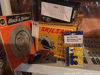 Photo shows boxed Skilsaw, Black & Decker blade in original packaging, hammer, hand plane and BrassCraft mini tube cutter on white shelf.