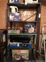 Two images of the black metal utility shelving unit with kitchen appliances and cookware on shelves.