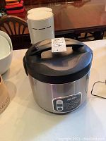 Aroma rice cooker with stainless steel finish and black lid and handle, digital control panel visible.