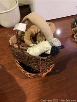 Rectangular wicker basket filled with draft stoppers, skeins of yarn in white and beige, and knitting needles.