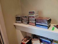 Stacked music CDs in jewel cases on a shelf including rock, pop, and classical music genres