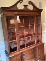 Full view of light mahogany Sheraton style china cabinet with glass upper doors and decorative pediment.