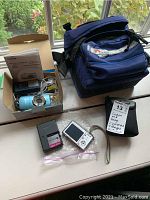 Canon PowerShot SD960 IS digital camera and charger with Sony Cybershot camera, charger and two LowePro camera bags shown outside boxes on table.