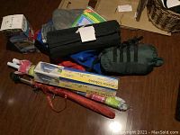 Camping gear items arranged on wooden floor including sleeping bag, mosquito net, cabana, umbrellas, and cloth bags.