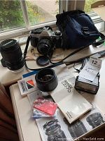 Overview of Canon AE-1 camera body, lenses, flash, filters, lens hood, manuals, and camera bag displayed on table