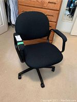Front view of black fabric rolling desk chair with padded armrests and caster wheels