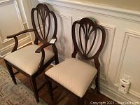 Pair of Sheraton style mahogany dining chairs shown from front. One chair has armrests (captain's chair) and both have beige upholstered seats.