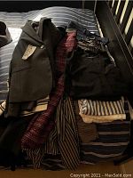 Various ladies clothing items including blazers, dresses, pants, tops, laid out on a striped bed.