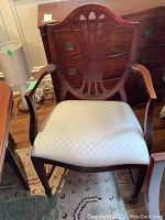 Clear photo of a captain's chair showing mahogany wood frame with a shield back and cream patterned fabric upholstered seat under daylight inside a room.