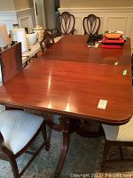 Full view of the table including chairs, showing tabletop with two extension leaves and polished mahogany wood.