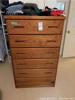 Front view of tall wooden dresser with six drawers and textiles on top.