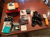 Wide view showing all items on table including GoPro HERO3+ Silver camera, cases, mounts, filters, Fitbit Versa with bands, first aid kit, and Kingston 5-in-1 card companion.